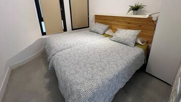 A bedroom with a bed, a wooden headboard, a potted plant, and two doors.