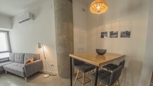 A modern living space with a grey sofa, a dining table with four chairs, a pendant light, and a concrete pillar. - Apartamento Granada Parque Ciencias 3000 (Granada)