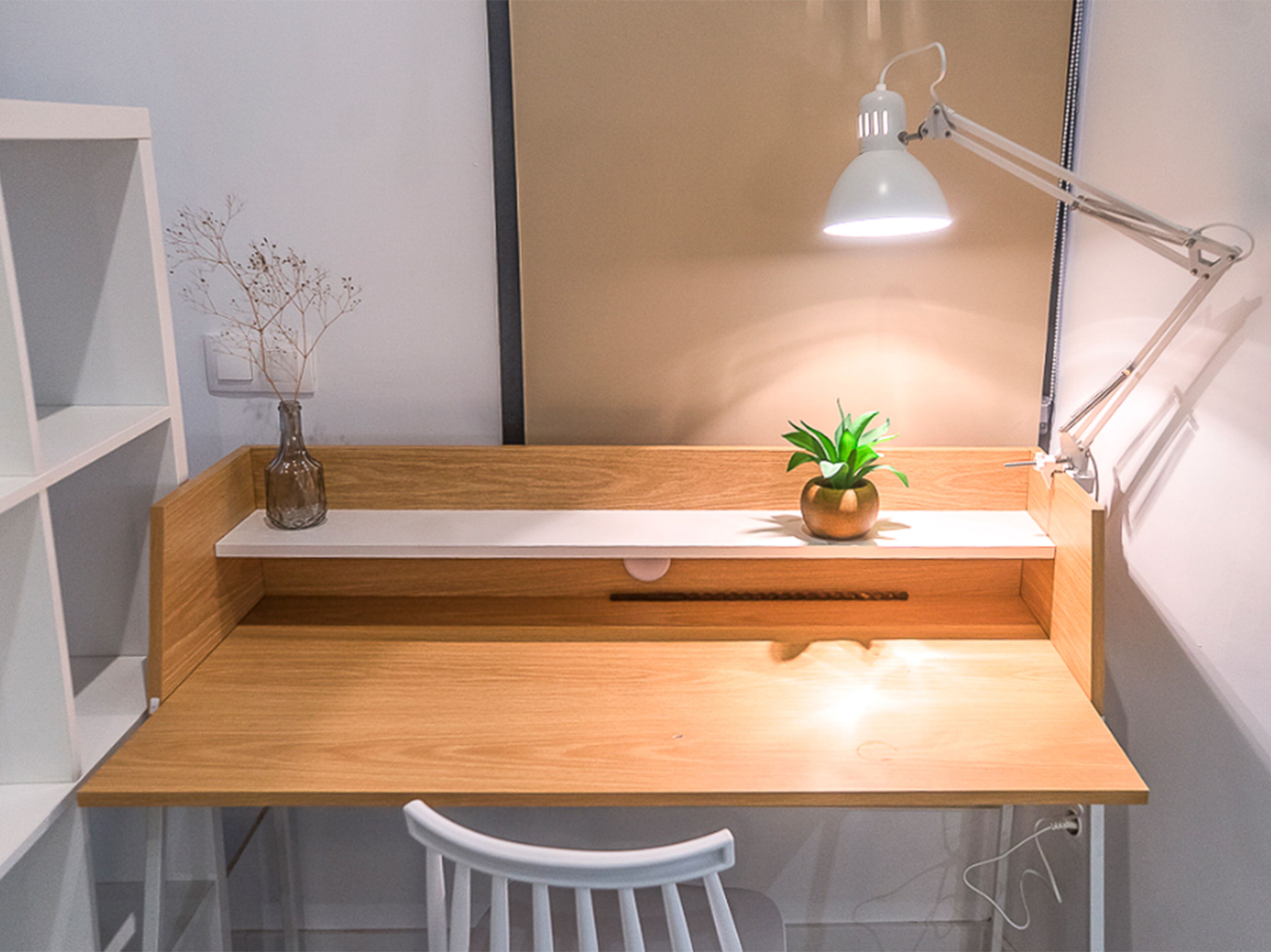 Een houten bureau met een witte stoel, een kleine plant in een pot en een bureaulamp.