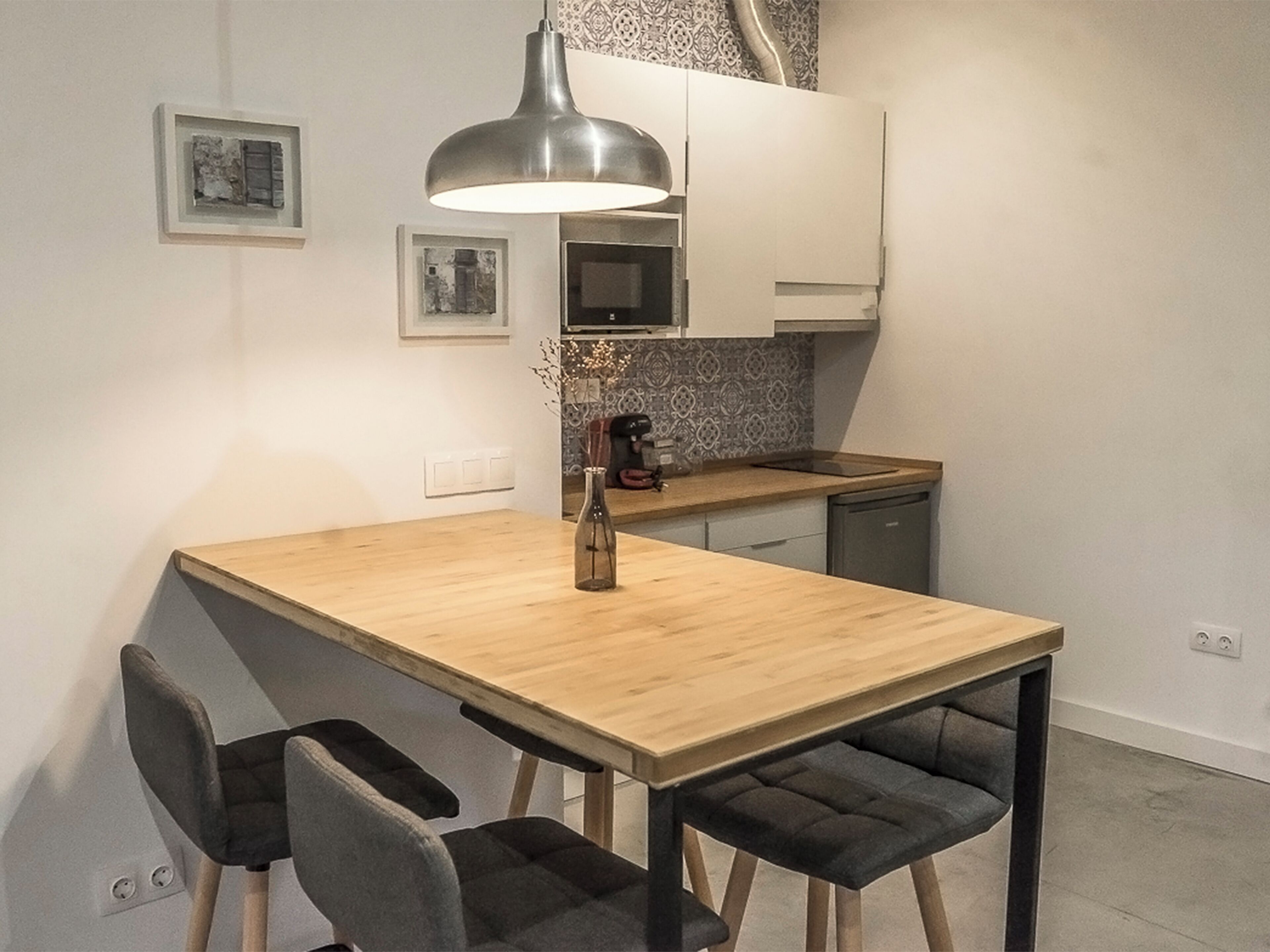 A modern kitchen with a wooden table, two chairs, a pendant light, and a coffee machine.