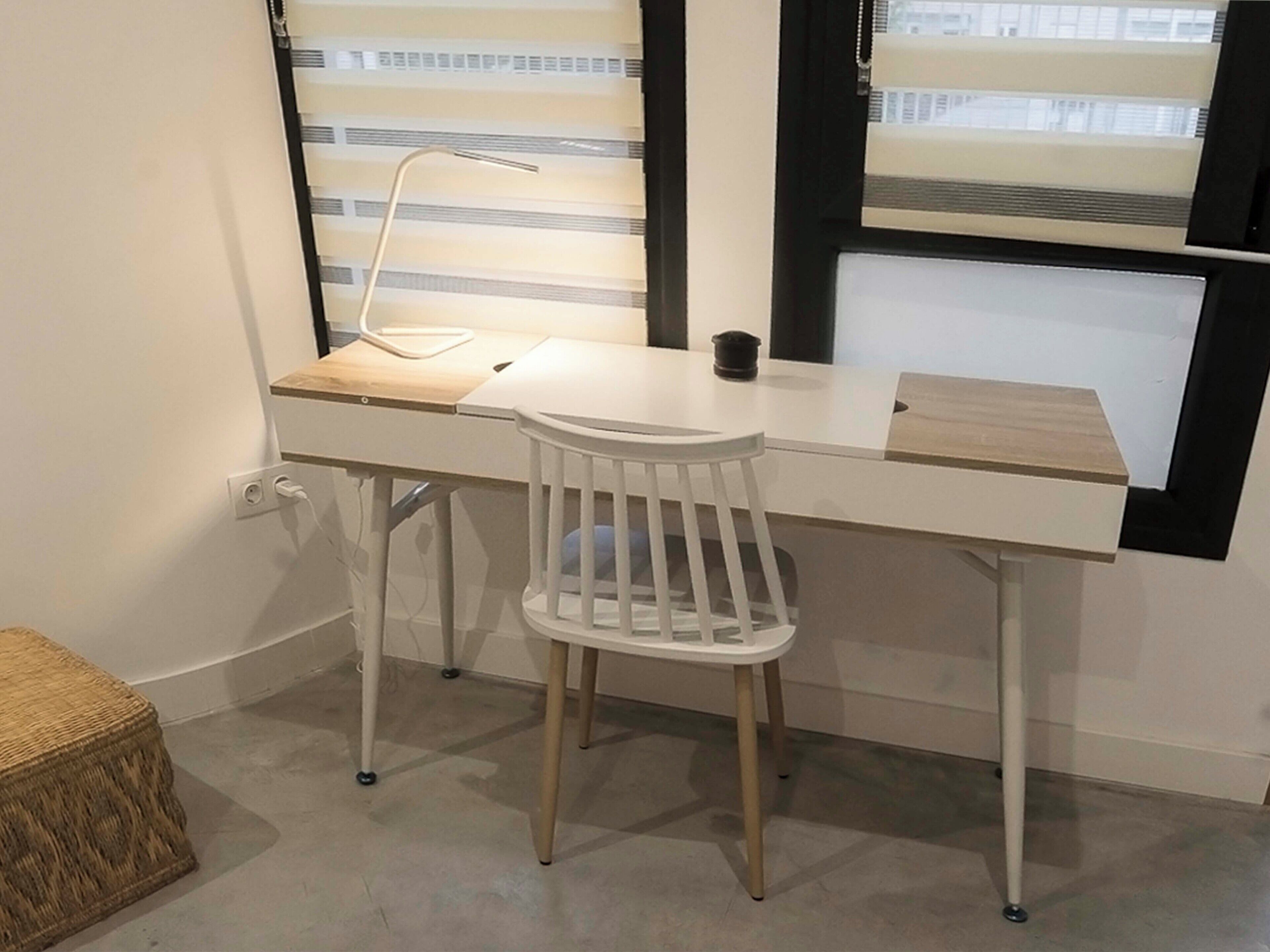 Un escritorio blanco con una silla, una lámpara y una mesita.