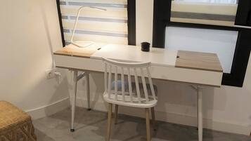 Un escritorio blanco con una silla, una lámpara y una mesita.