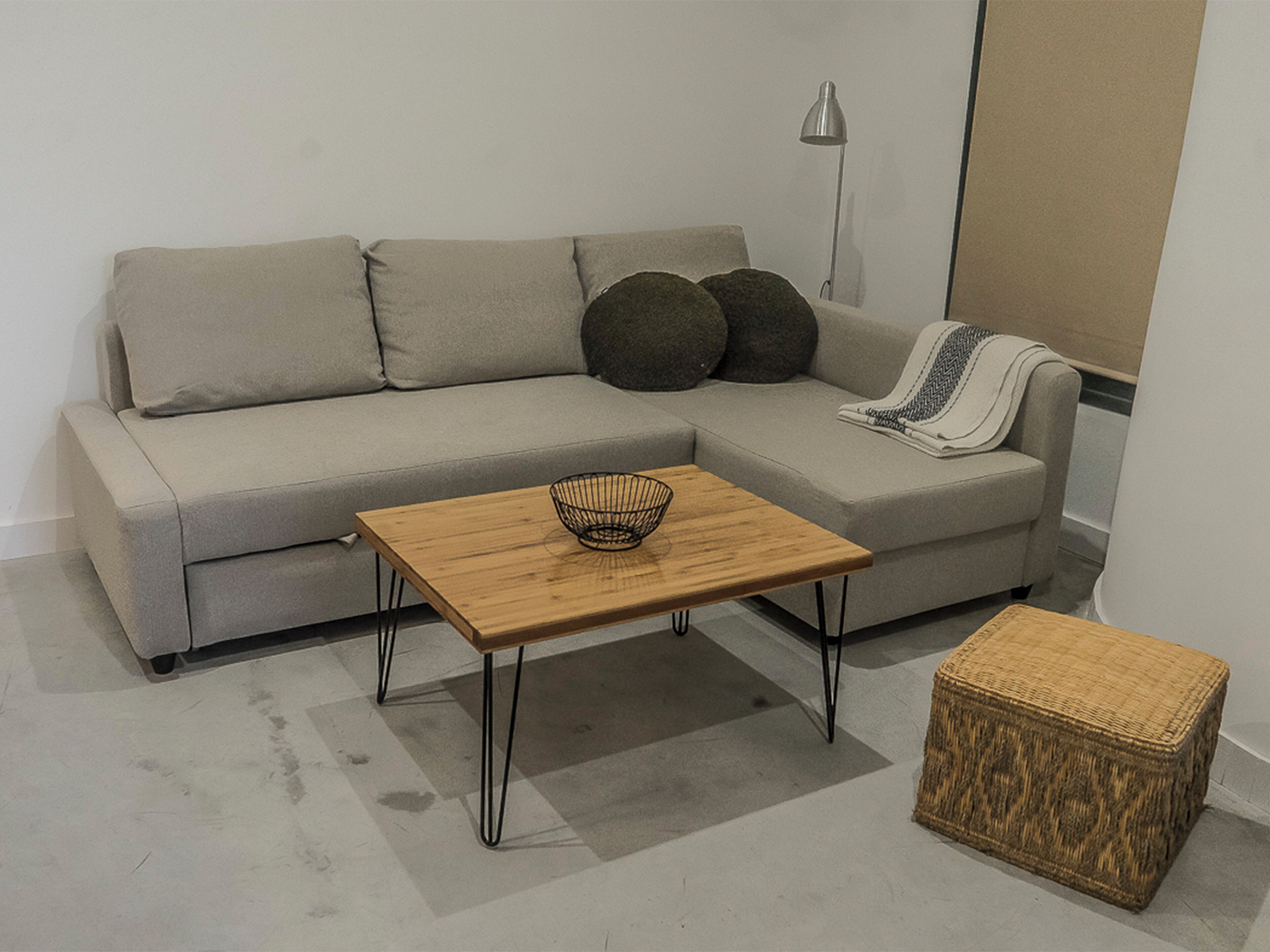 Een moderne woonkamer met een grijze bank, een houten salontafel met een draadmand en een rieten poef.