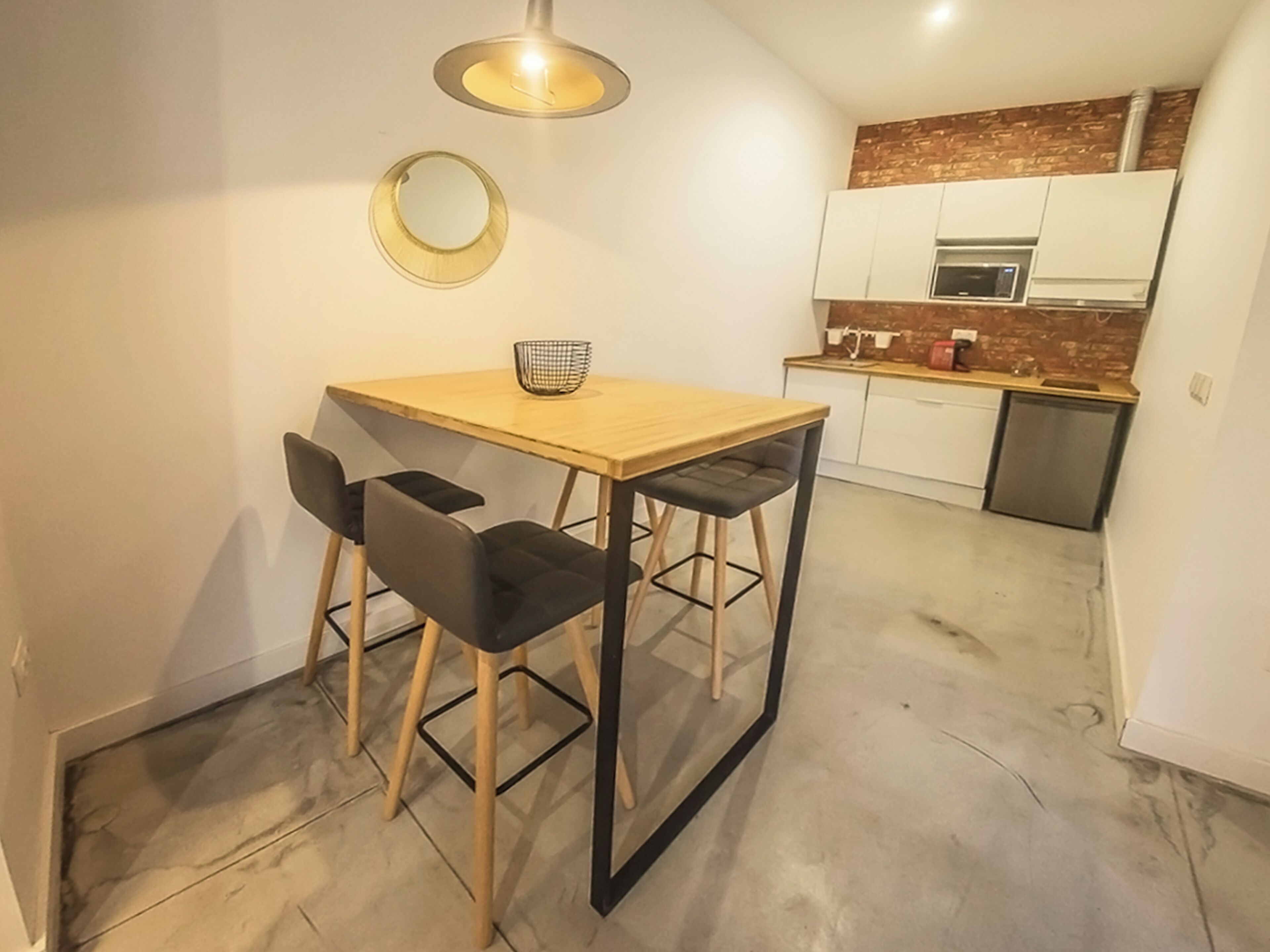 Une cuisine compacte avec un coin repas, comprenant une table en bois, deux chaises, un petit miroir rond et un luminaire moderne.