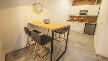 A compact kitchen with a dining area, featuring a wooden table, two chairs, a small round mirror, and a modern light fixture.
