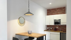 A modern kitchen with white cabinets, a brick accent wall, a wooden dining table with black chairs, a pendant light, and a microwave. - Apartamento Granada Parque Ciencias 3000 (Granada)