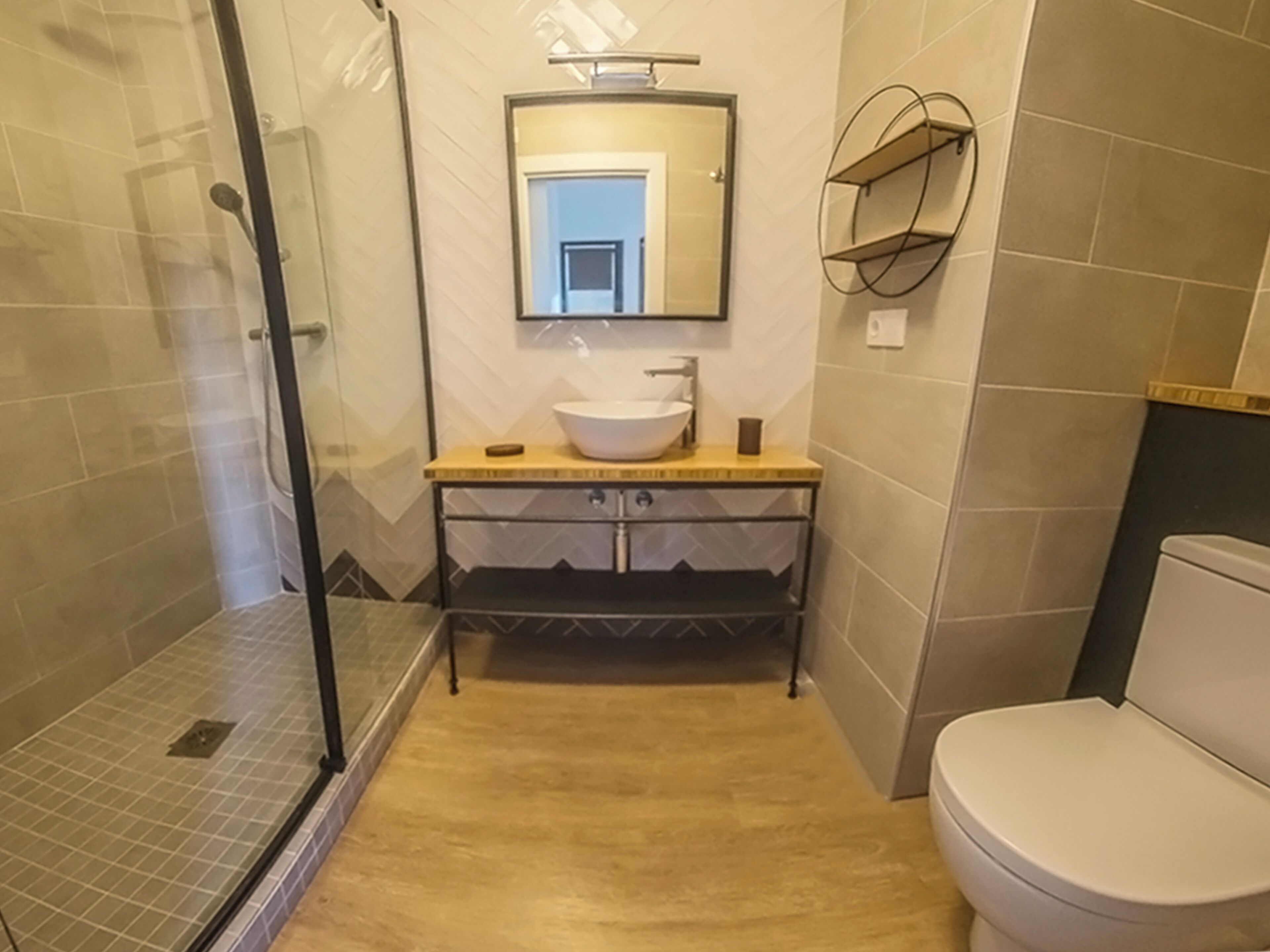 A bathroom with a glass shower enclosure, a sink with a mirror above it, and a toilet.
