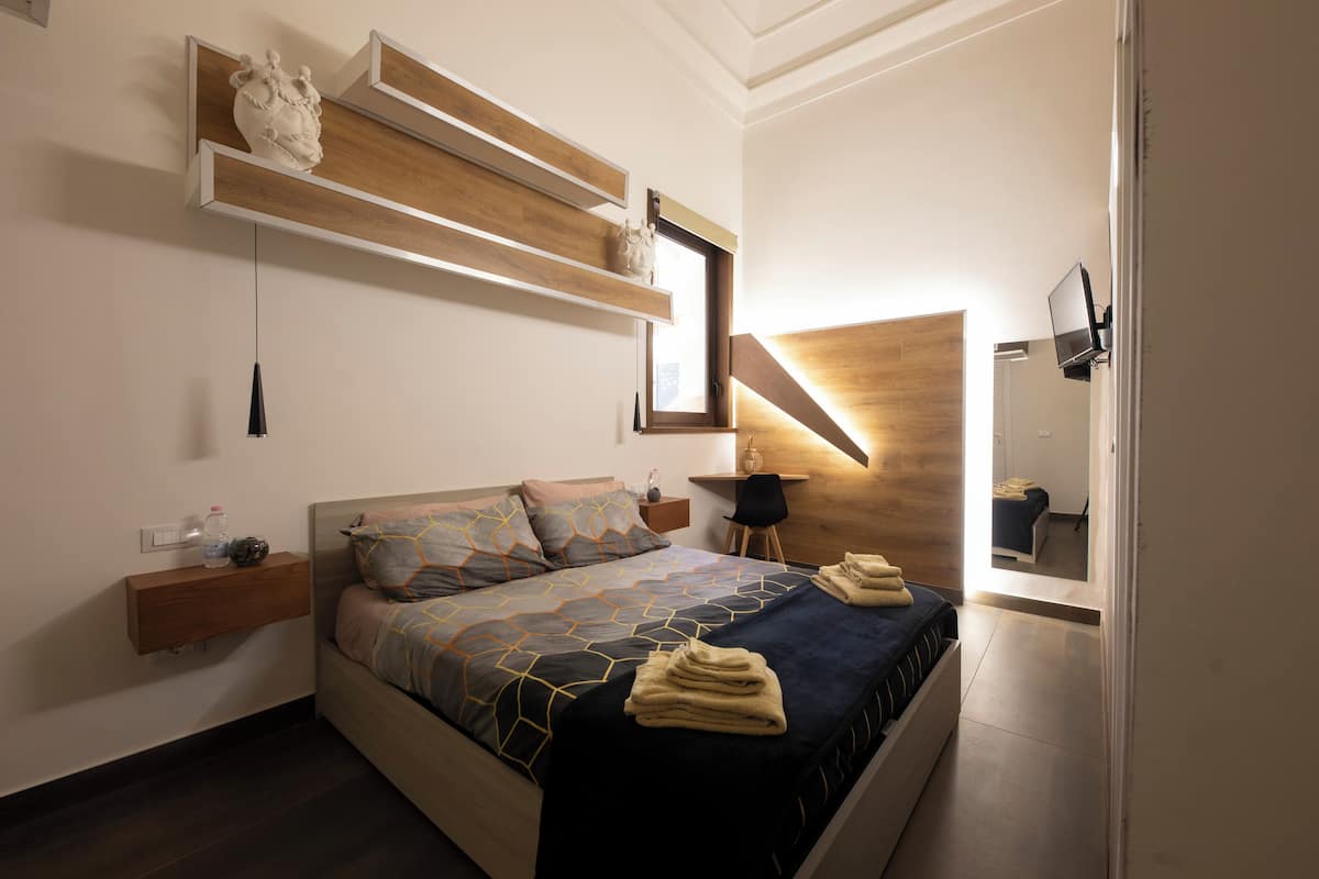 A modern bedroom with a bed, wooden headboard, bedside tables, and a TV mounted on the wall.