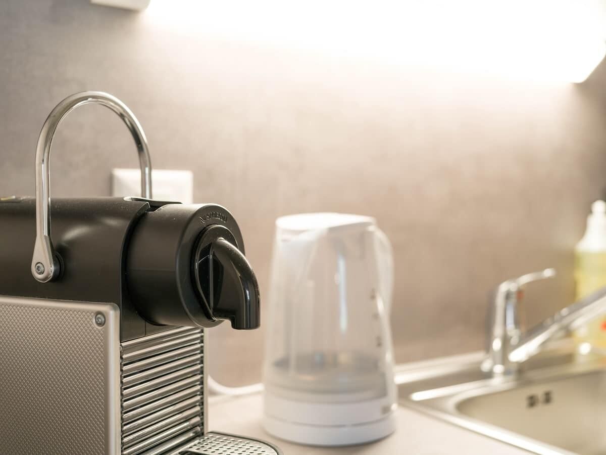 A kitchen with a coffee maker, a kettle, and a sink.