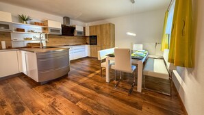 Una cocina moderna con suelo de madera, armarios blancos y un comedor con mesa y sillas.