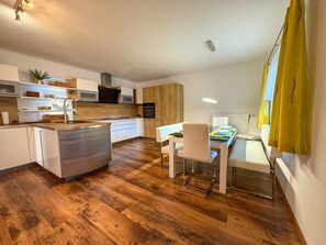 A modern kitchen with wooden flooring, white cabinets, and a dining area with a table and chairs. - Apartment Leander with Mountain View, Private Terrace and Wi-Fi (Kleinsölk)