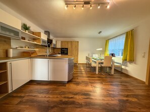 A modern kitchen with a central island, wooden flooring, and a dining area with a view. - Apartment Leander with Mountain View, Private Terrace and Wi-Fi (Kleinsölk)