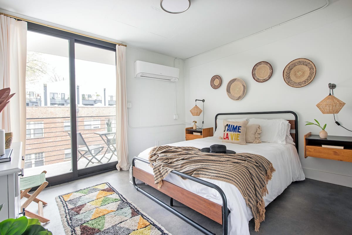 A bedroom with a bed, a desk, a chair, a window with curtains, and a balcony.