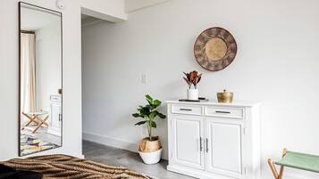 Una habitación con un espejo grande, un armario blanco, una cesta de mimbre con una planta y una alfombra tejida.