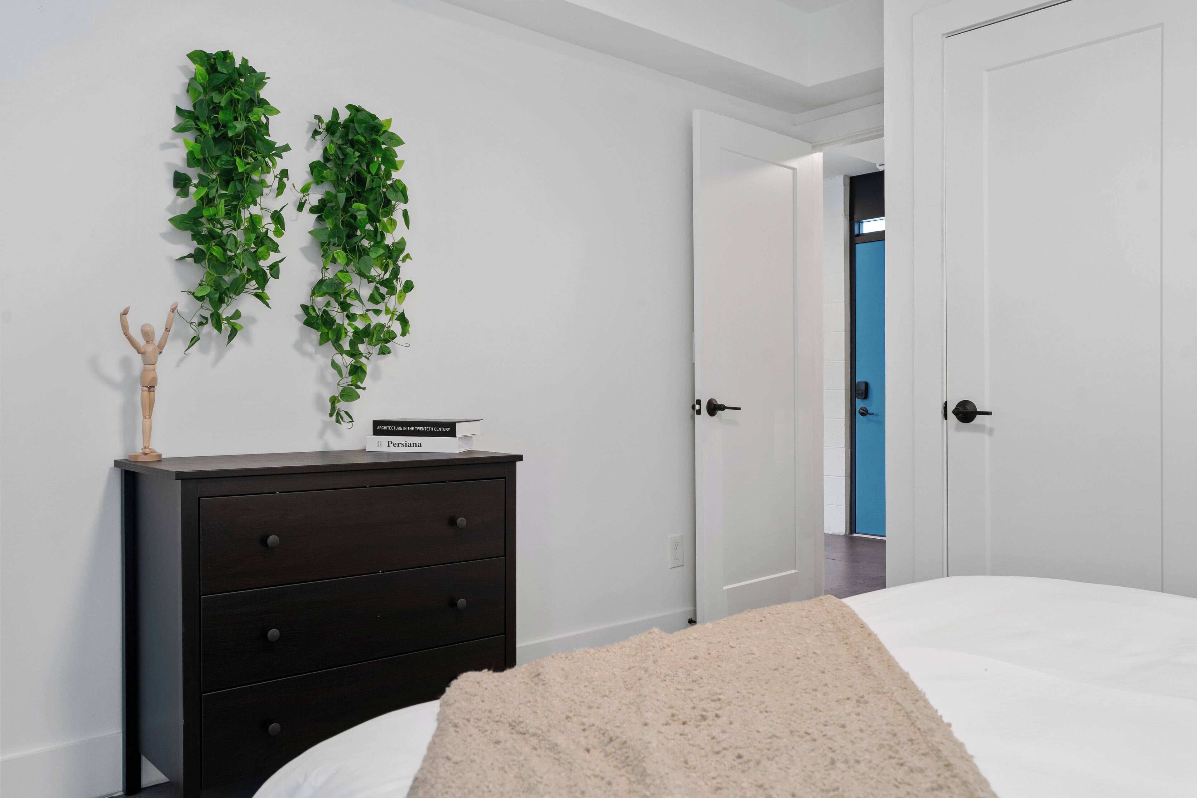 A bedroom with a bed, a dark dresser, and two green plants on the wall.