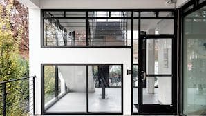 Entrada de un edificio moderno con puerta de vidrio, escalera de metal y vista al exterior.