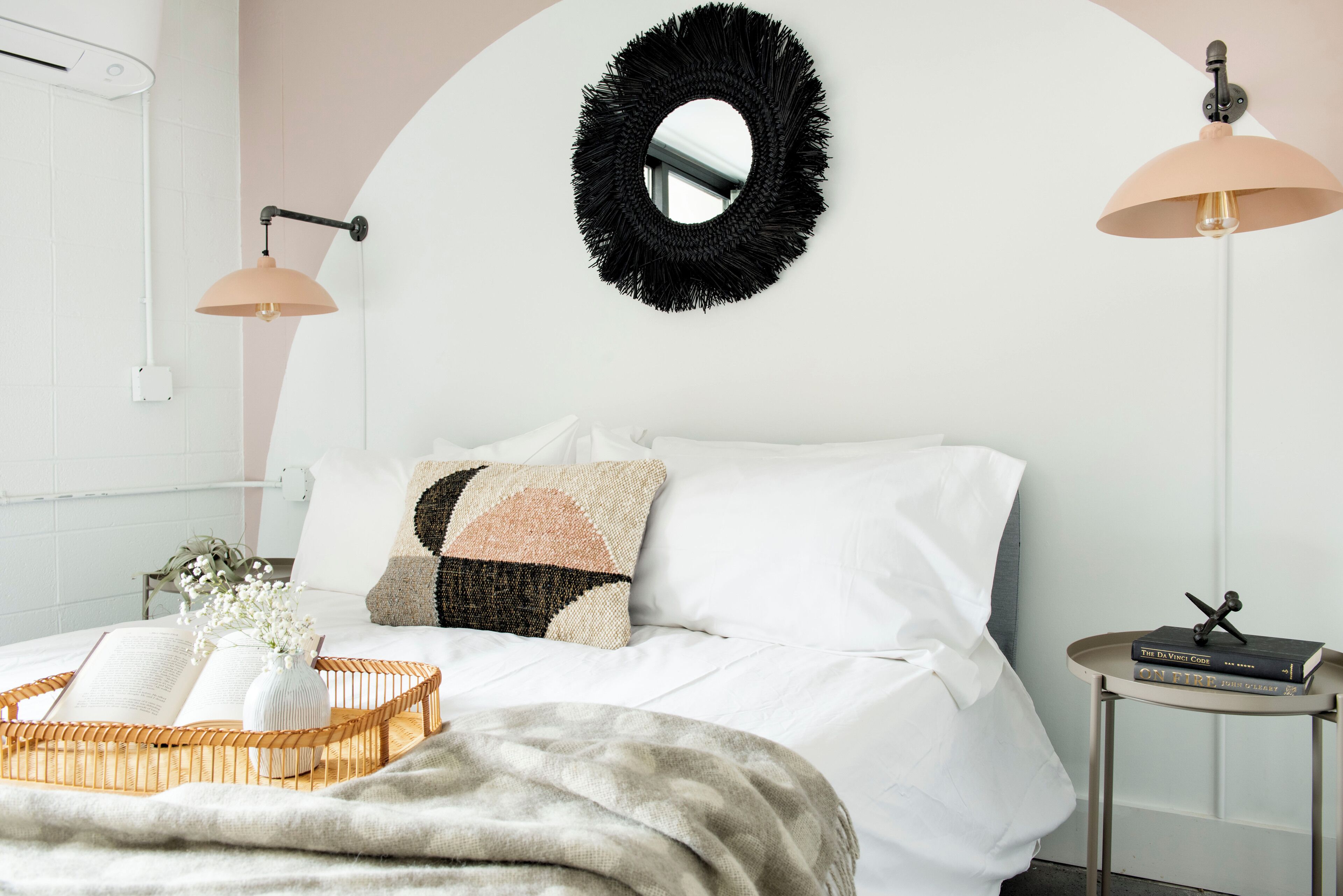 A neatly arranged bedroom with a bed, bedside table, and a wall-mounted mirror.