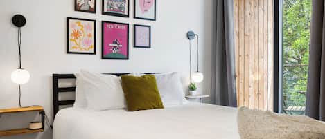 Un dormitorio moderno con una cama, mesitas de noche y una ventana con vistas a zonas verdes.