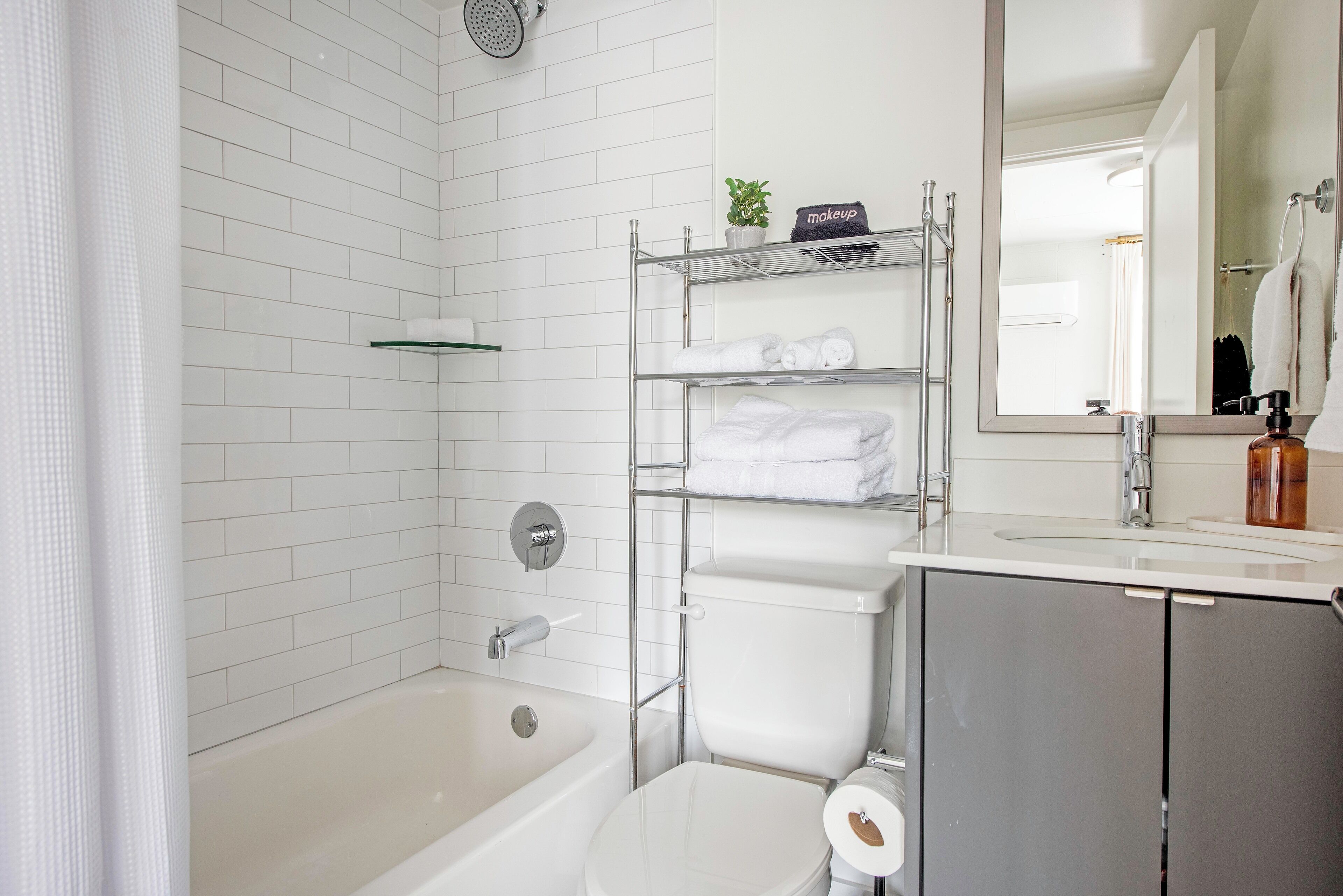 Une salle de bain moderne avec une douche carrelée de blanc, une baignoire, des toilettes et un meuble-lavabo avec un miroir.