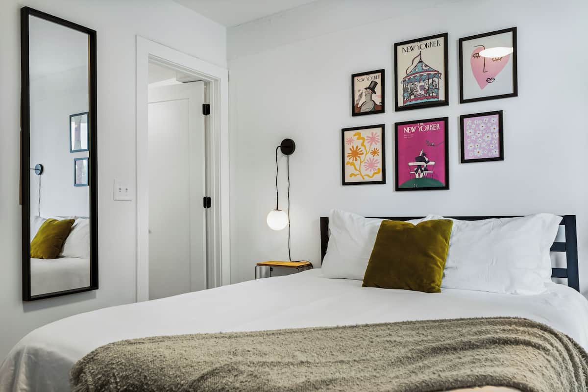 A bedroom with a large bed, a bedside table, a lamp, and wall art including framed pictures and a mirror.