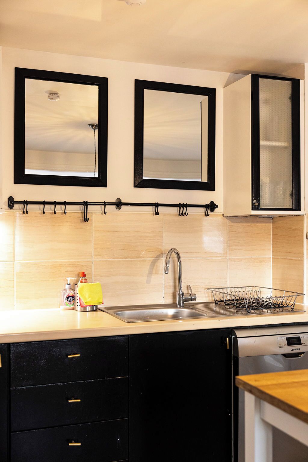 A kitchen with a sink, two mirrors, a dish rack, and a cabinet.