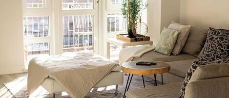 Un salon chaleureux avec un canapé, une table basse ronde et un lit recouvert d’une couverture blanche.