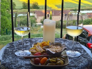 Une table avec deux verres de vin blanc, une bougie et une assiette de nourriture comprenant des cornichons, des tomates et des crackers.