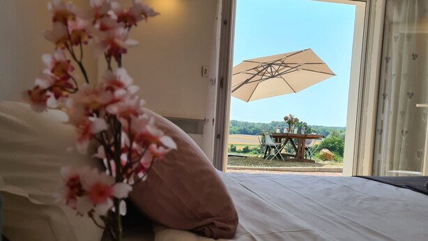 Un dormitorio con cama, un florero con flores y vistas a una mesa y sombrilla exteriores.