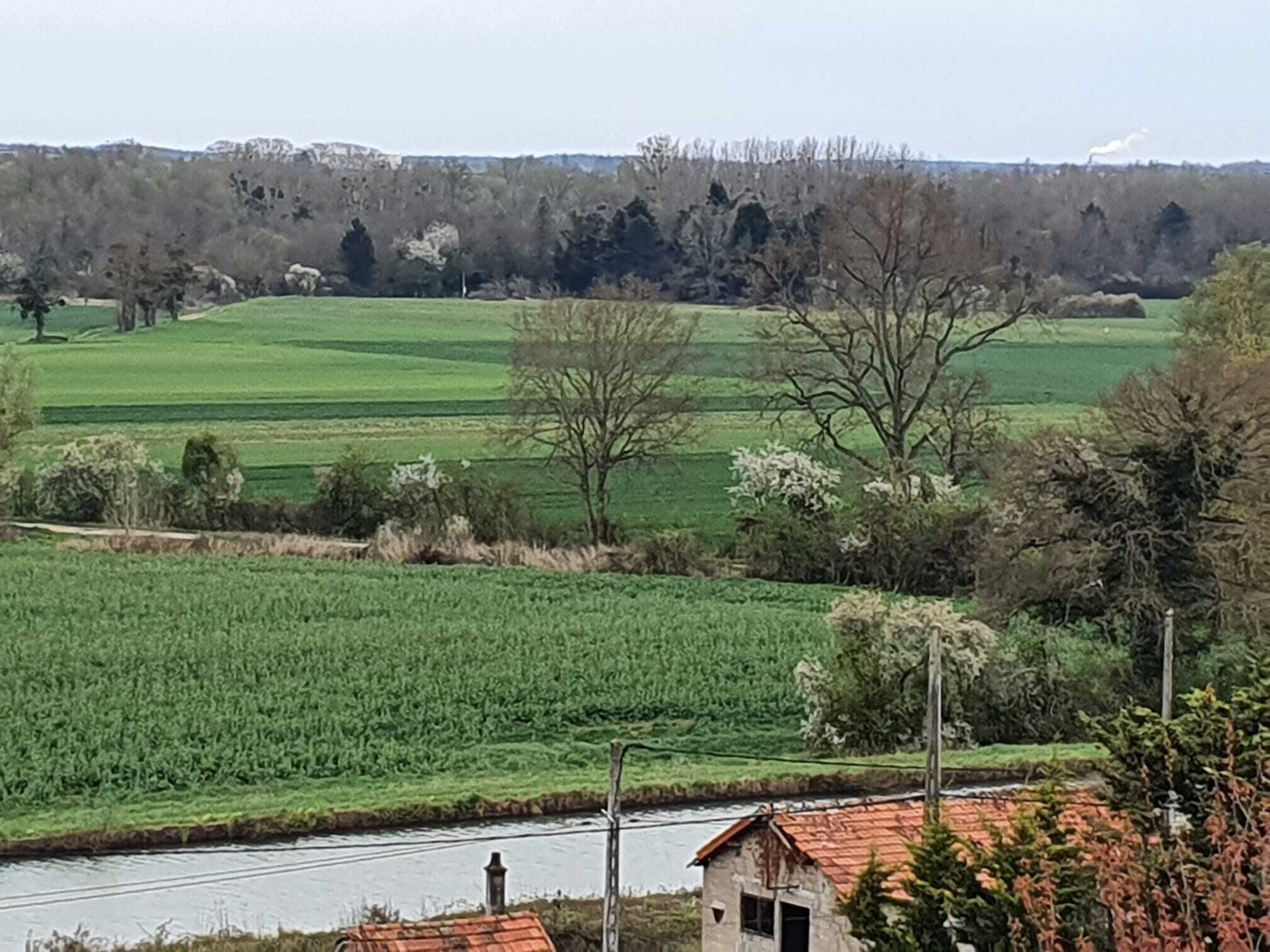Landelijk landschap met velden, een rivier en een klein gebouw met een rood dak.