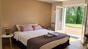 Un dormitorio con una cama grande, una mesita de noche con una lámpara y vistas al exterior a través de un ventanal.