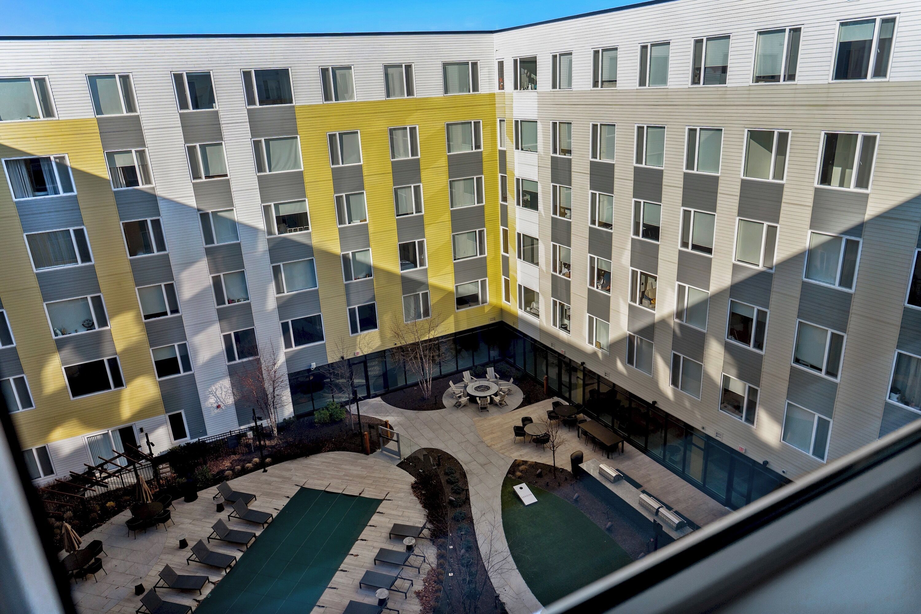 Un edificio de varios pisos con un patio que cuenta con asientos exteriores, una piscina pequeña y un brasero.