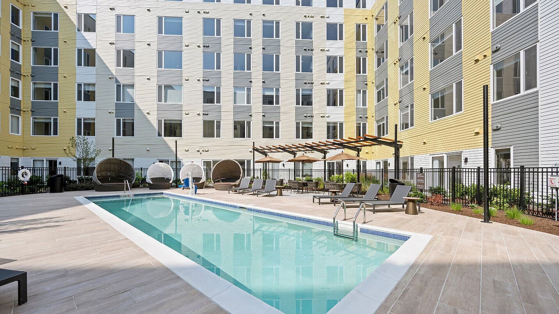 A modern apartment building with a rooftop pool, outdoor seating, and a pergola.