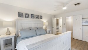 Una camera da letto con un letto, comodini, una ventola a soffitto e opere d'arte alle pareti.