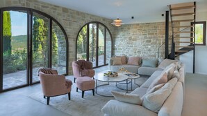 Ein geräumiges Wohnzimmer mit Steinsäule, großen Fenstern, einer Couch, Sesseln und einem Couchtisch.