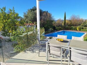 A poolside area with a table and chairs, a clear blue pool, and surrounding greenery. - Village house with pool, separate apartment & mountain views (Querença)