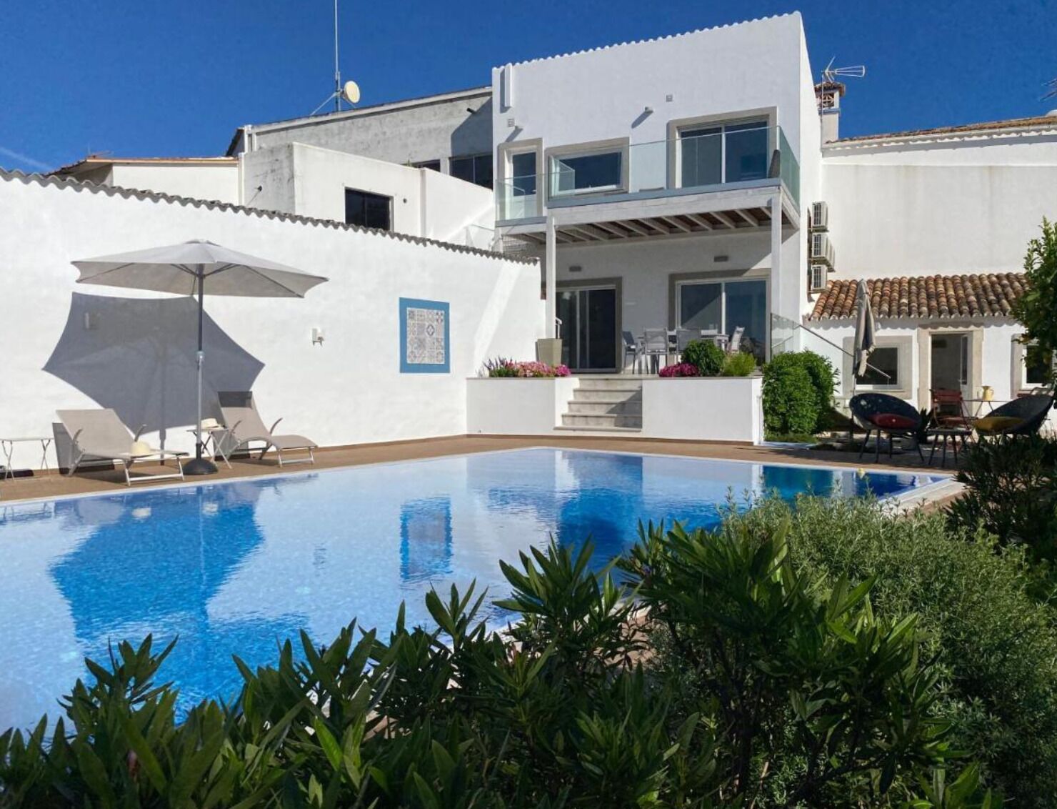 A modern two-story house with a swimming pool, outdoor seating, and a garden.