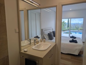 A modern bathroom with a double sink, a large mirror, and a view of a bedroom with a bed and towels. - Village house with pool, separate apartment & mountain views (Querença)