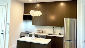 A modern kitchen with dark cabinetry, a stainless steel refrigerator, a central island, and a pendant light. - Luxury Mountain Retreat with Scenic Balcony Views (Cashiers)