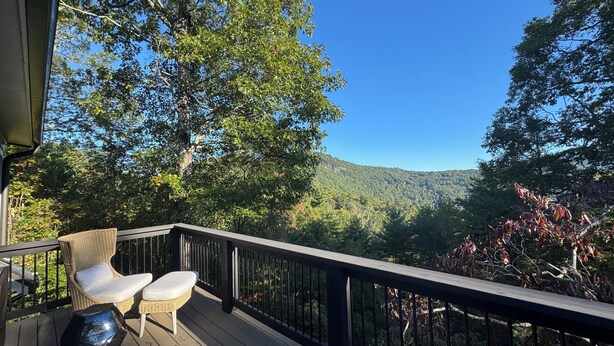 A wooden deck with wicker chairs and a glass table, overlooking a forested hillside. - Luxury Mountain Retreat with Scenic Balcony Views (Cashiers)