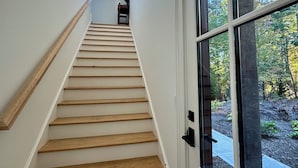 A staircase with wooden steps and white walls, leading to a door with a view of trees. - Luxury Mountain Retreat with Scenic Balcony Views (Cashiers)