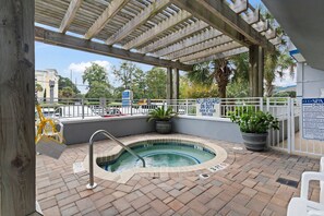 Een buitenzwembadgedeelte met een overdekte pergola, een jacuzzi en een bord met de waarschuwing dat er geen badmeester aanwezig is.