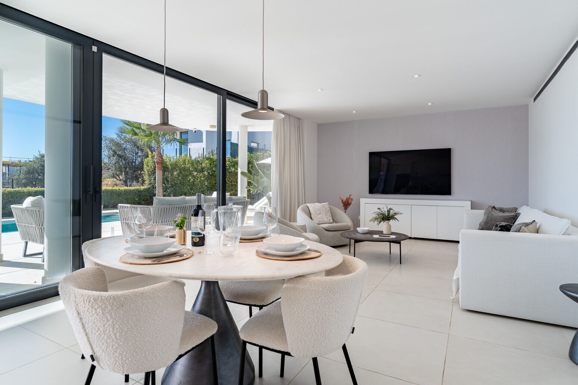 A modern living room with a dining area, large windows, and a flat-screen TV.