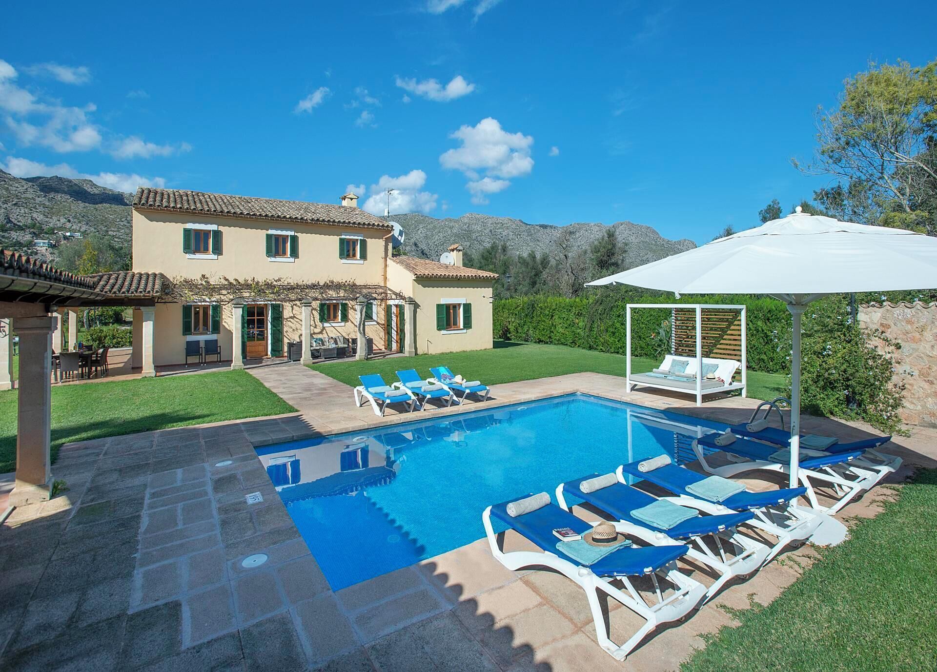 Ein Poolbereich mit Liegestühlen und einer Pergola, umgeben von einem gepflegten Rasen und einem Haus mit Ziegeldach.