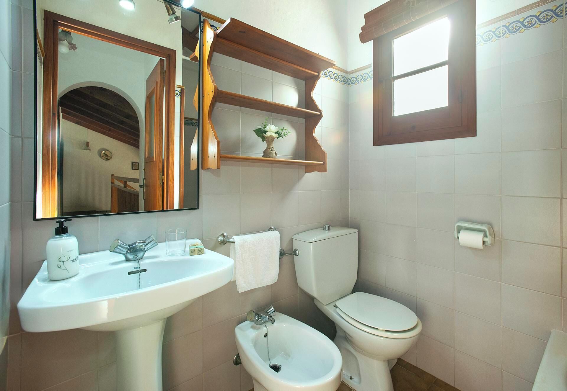 A bathroom with a sink, mirror, toilet, bidet, and a window.