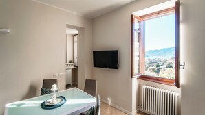 Un comedor con mesa de vidrio, sillas, una vela y un televisor en la pared.