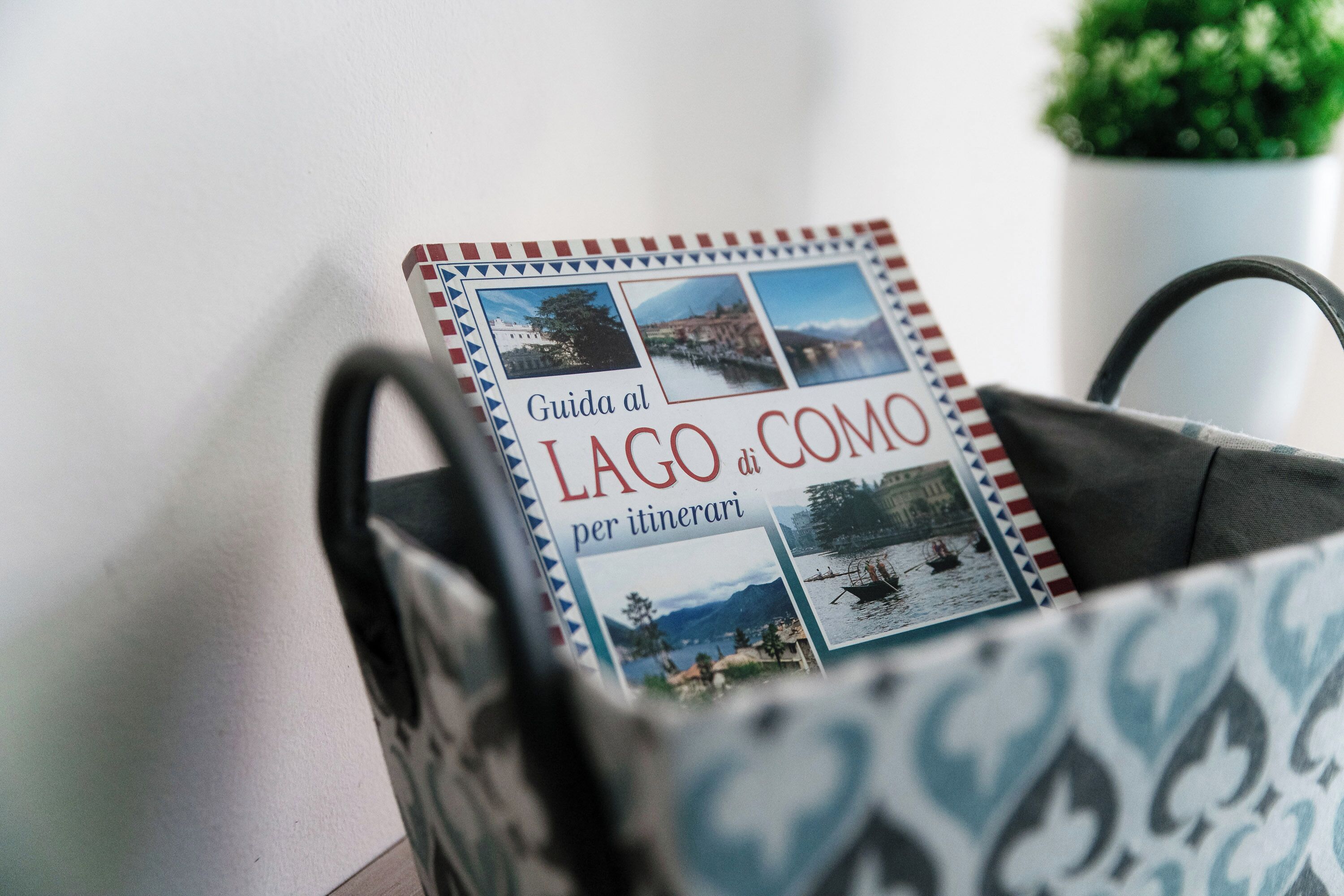 A travel guidebook titled "Guida al Lago di Como per itinerari" in a patterned bag.