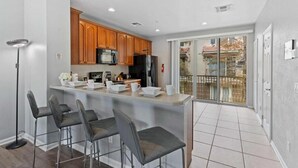 Una cocina moderna con armarios de madera, una isla central con taburetes altos y un ventanal corredero que da a un balcón.