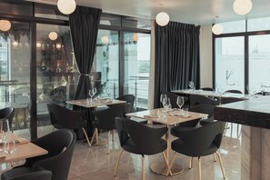 Ein modernes Restaurant mit schwarzen Stühlen, runden Tischen und großen Fenstern, die einen Blick auf die Stadt bieten.
