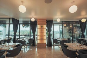 Een modern restaurantinterieur met een centraal houten schap, zwarte stoelen en ronde hanglampen.