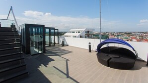 Eine Dachterrasse mit einem gläsernen Anbau, einer Sitzecke mit blauem Baldachin und Blick auf eine Stadtlandschaft.